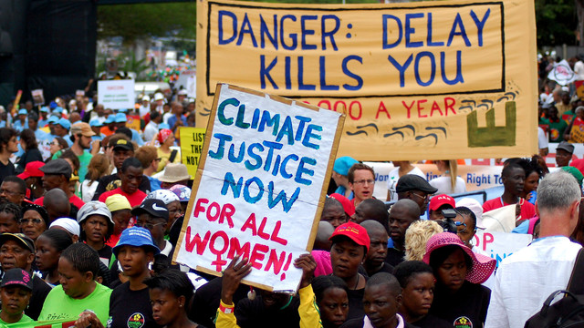 A host of people carrying placards and banners, with a prominent banner that says: "Danger: delay kills you".