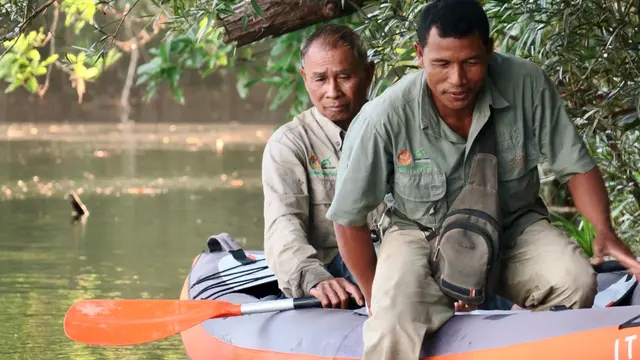 Two men in a dinghy out on water; one holding an oar.