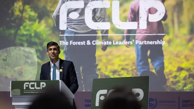 A suited man stands at a podium making a speech.