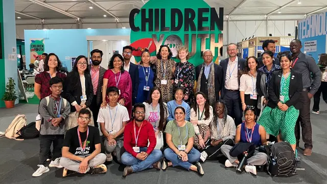 A group of people, largely young people, gather to pose for a photo, inside a conference venue.