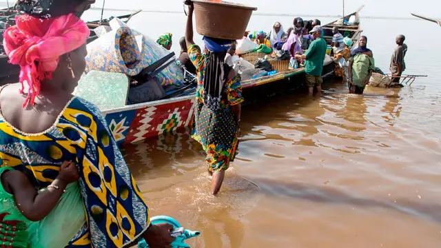 Women wade out to load a boat with cargo