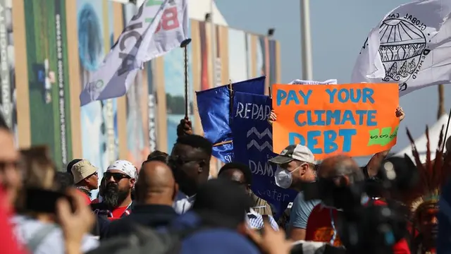 Mass of people walking with flags and posters. A sign reads "pay your climate debt"