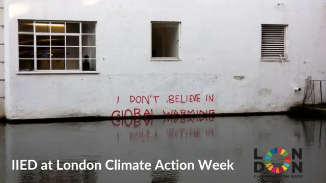 Text saying "I don't believe in global warming" written on a wall beside a canal, with the water overlapping the bottom of the words.