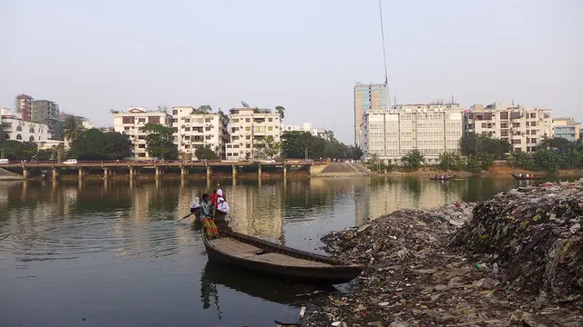 A boat on a river next to a pile of garbage with buildings in the background.