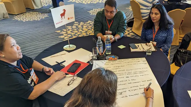 People sitting on a round table and writing notes on a poster.