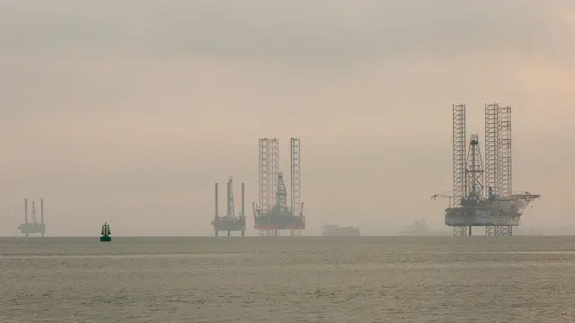 A misty seascape with rigs protuding out of the water.