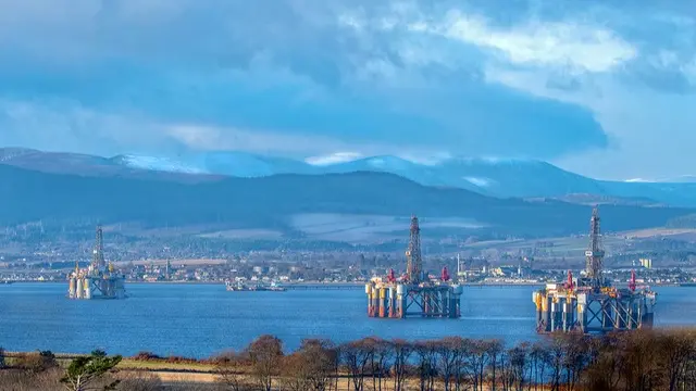 Oil rigs in water with mountains in background.