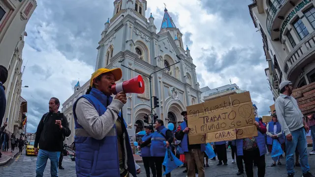 Man at a protest holds a megaphone leading a crowd, holding signs.