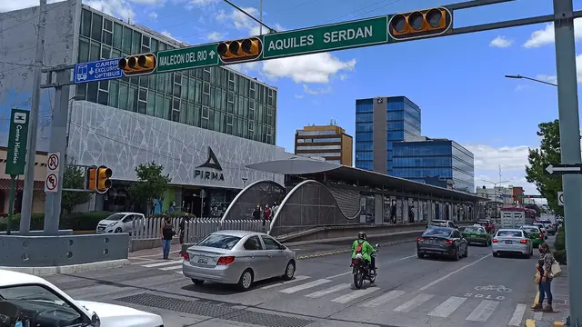 A woman waits beside a busy intersection as cars and motorbikes drive past. 