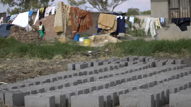 Rows of grey bricks on the ground outside a house. In the background, washing is hanging on a line.