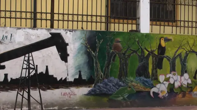 A mural on a wall depicting, on the left, an oil field in grey muted colours and, on the right, trees, birds, plants and wildlife in vibrant colours.