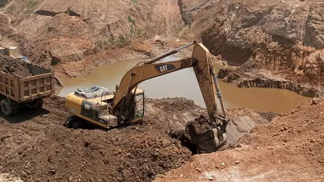 A digger in a mining quarry digs earth and transfers it to a lorry just behind it.