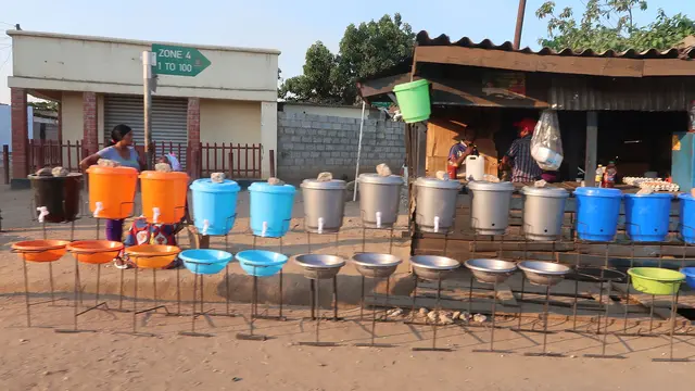 A row of multicoloured containers filled with water beside a dusty road. 