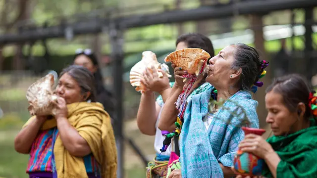 Indigenous Women performing a Tlalmanalli opening ceremony. They are wearing traditional dress and blowing into sea shells.
