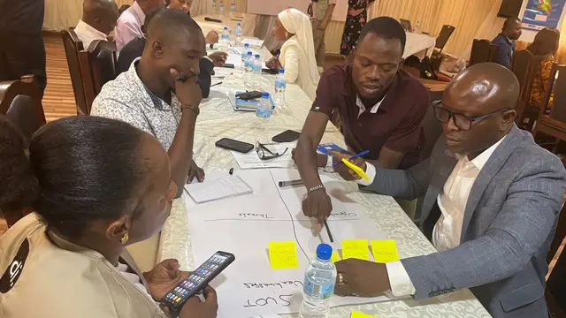 Four workshop participants are sitting at a table, discussing and writing things down on post-it notes.