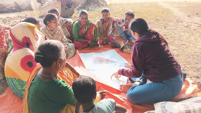 Women sitting in a circle outside, discussing and reading large print outs.