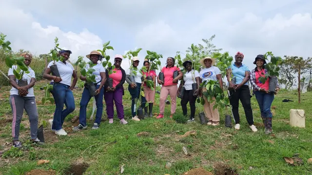 Group of ASOM women members holding plants in a field, smiling at the camera.