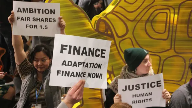 Protestors at a cafe sit-in near COP21. They are holding signs that say 'Ambition fair shares for 1.5', 'Finance adaptation finance now!' and 'Justice human rights'.