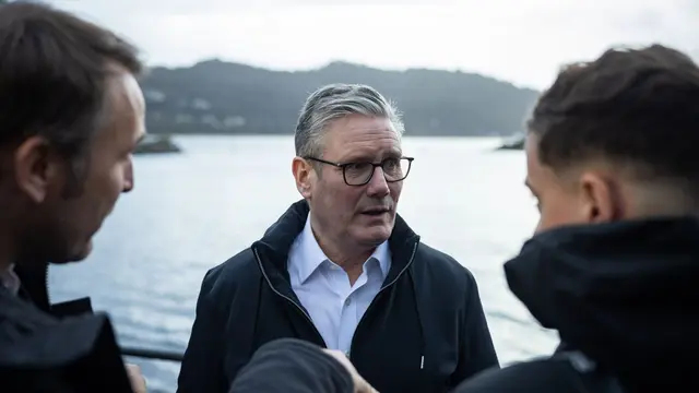 Image of Keir Starmer talking to two journalists while on a boat.