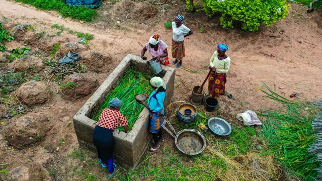 Women from local community gathered around a water tank, washing vegetables.