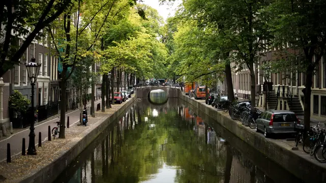 Image of a canal in Amsterdam, with cars and bikes parked on the banks and trees covering the sky.