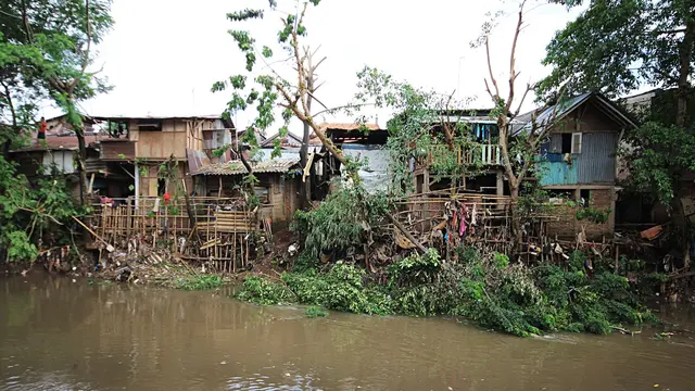 Informal settlement with torn-down houses on the edge of a body of water in Jakarta.