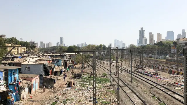 Informal settlement in Mumbai situated next to train tracks with various electric wires going above it.