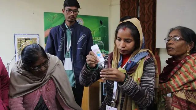 Group of women wearing traditional Indian dress gathered around as one of them is testing the quality of water.