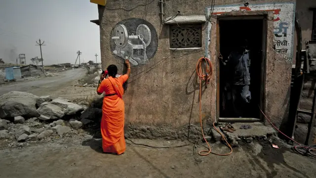 Woman worker in a stone quarry wearing a bright orange saree is making a phone call using a land line outside a building.
