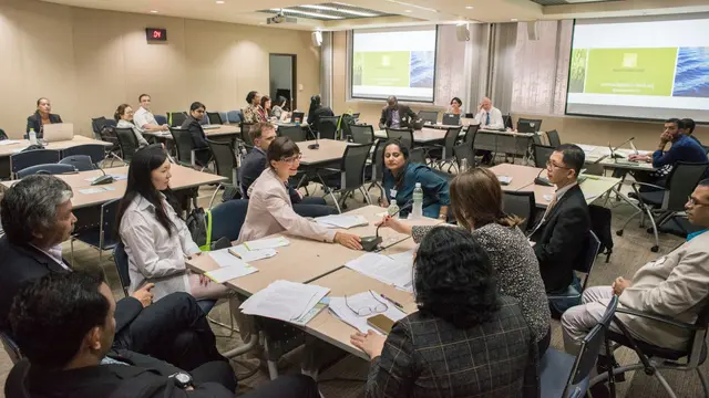 People gathered at a table in a conference room, talking and gesticulating.