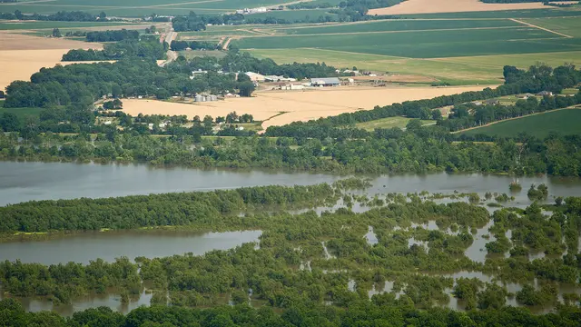 An aerial view of a river that has flooded the surrounding area, showing fields and houses partly submerged by water.