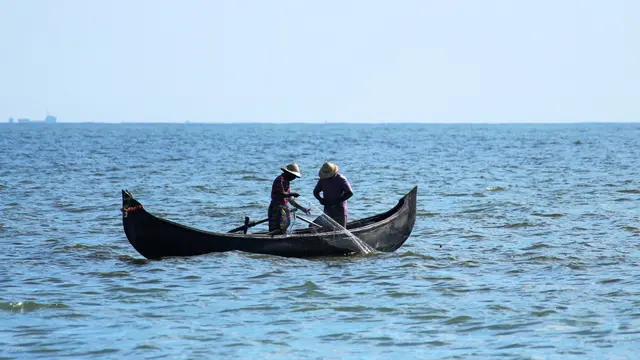 Two people on a fishing boat in India, catching fish with a net.