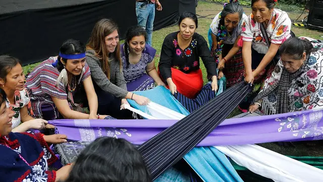 Indigenous women’s groups perform a Tlalmanalli ceremony in Mexico. They are sitting in a circle, wearing traditional clothing and grabbing colorful cloths and pulling them.