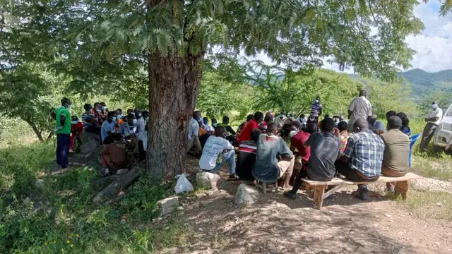 Community members from Zambia gathered next to a tree, sitting down and discussing.