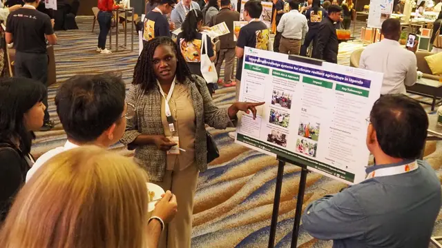 Person standing next to a printed out poster, pointing and speaking. Other people are gathered and listening.