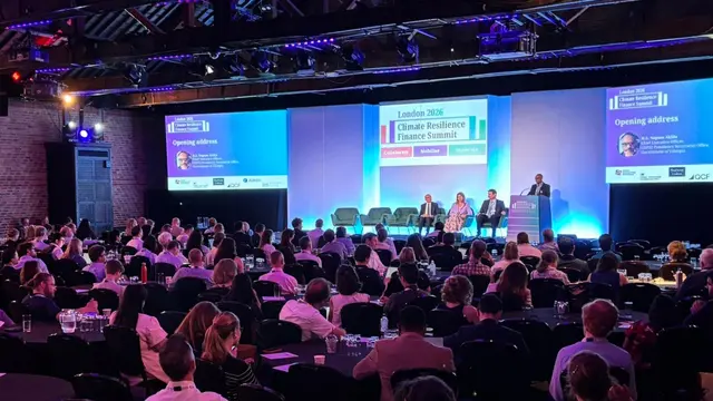 Panel discussion during the opening plenary of the London Climate Resilience Finance Summit 2026. Four speakers are standing on stage while the audience watches. A big screen is projecting the summit logo on the background.
