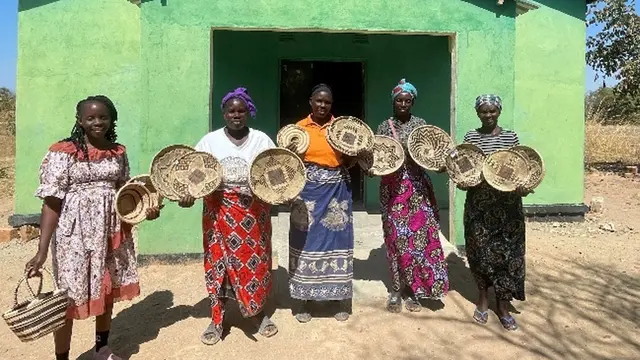 Five women stand in front of a building holding up large handcrafted baskets.