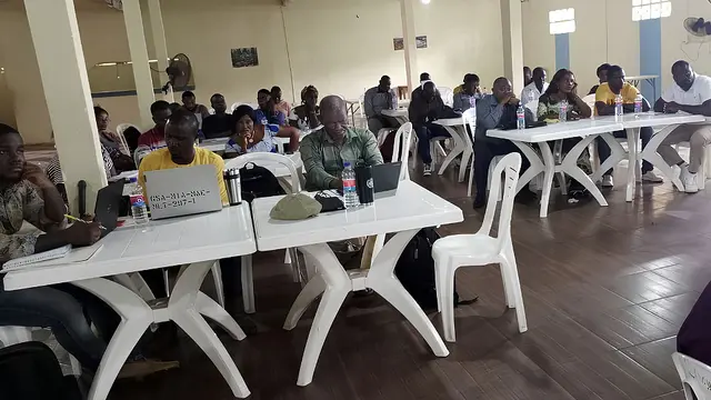 Men and women sit inside at tables writing and discussing with one another.