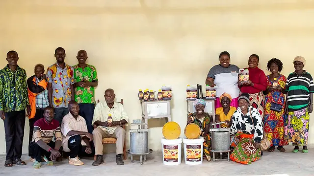 A group of men and women line up for a posed photo alongside large pots of honey.