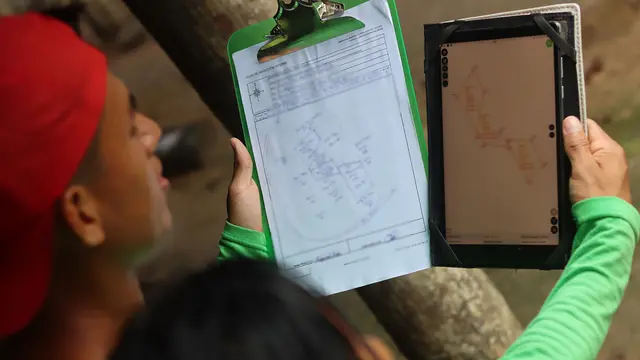 Two people look at a clipboard and an electronic tablet held up alongside one another.
