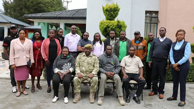 A group of smiling men and women line up for a posed group photo in front of a building.
