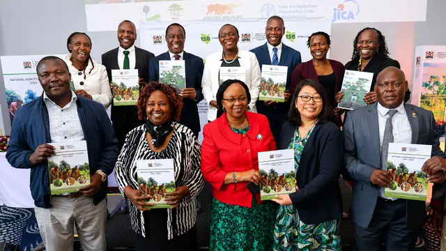 A group of smiling men and women line up for a posed group holding up booklets.