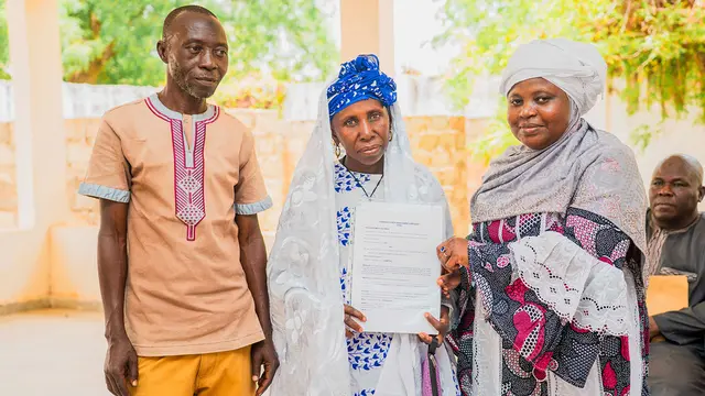 Three people pose for a photo, with the man in the middle holding up pieces of paper. 