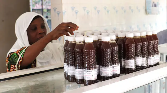 A woman reaches up to a shelf on which are stacked bottles of honey.