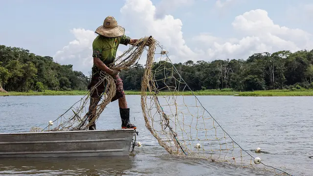 A man on a small boat maintains his balance as he draws in a net.