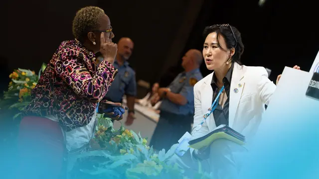 Two people with lanyards hanging from their necks engage in a discussion.