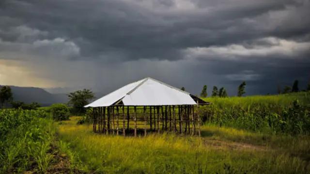A church under construction sits on a verdant green field with dark grey storm clouds behind. 