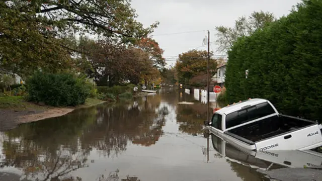 A pick up truck lies mostly submerged under a water in a flooded street. 