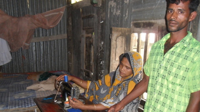 Bangladeshi man stands next to a woman who is working on a sewing machine