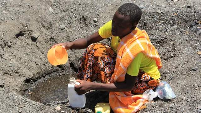A woman scoops water in a dry riverbed